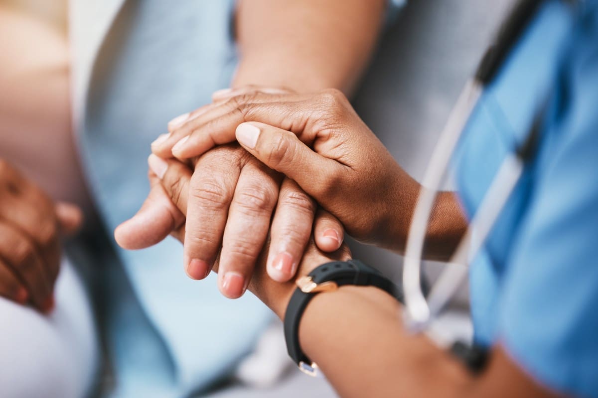 Healthcare worker comforting a patient's hands.