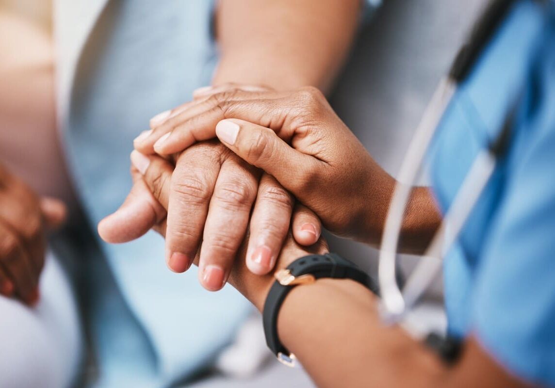 Healthcare worker comforting a patient's hands.